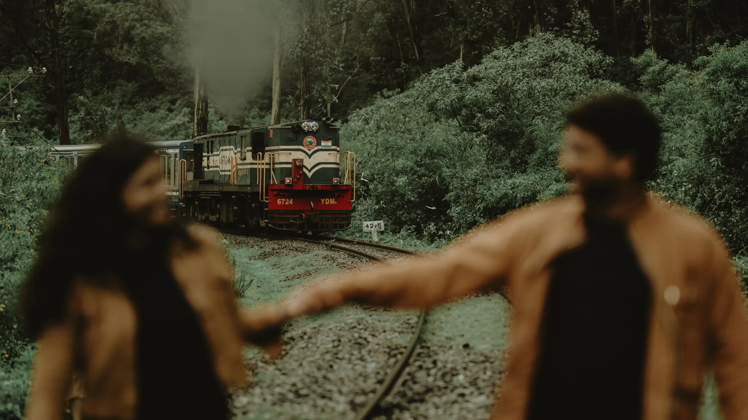 A couple holding hands and enjoying their moment as a train approaches, surrounded by lush greenery on both sides.🏢 Yuvi Studio Fotography & Film Making 📷 Best couple Photo shoot studio 📍 Velayuthampalayam, Karur
