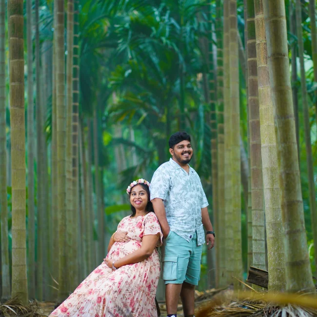 Yuvi Studio maternity photoshoot A mom-to-be in a pink floral dress and crown sits, while her husband stands behind her in a blue shirt π’ Yuvi Studio Fotography & Film Makingπ· Best Maternity Photographers π Velayuthampalayam, Karur