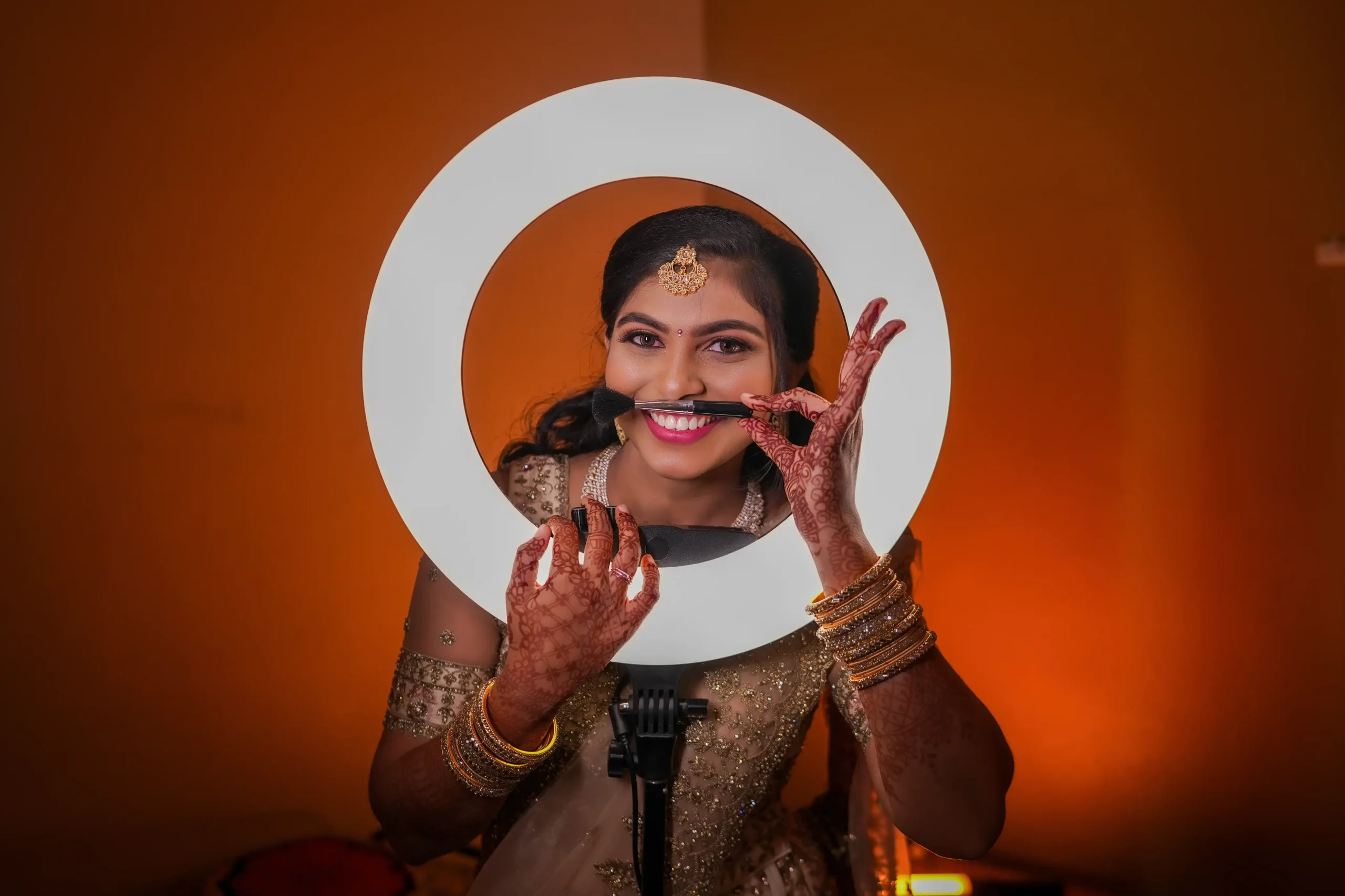 Tamil bride Preethi in lehenga posing with ring light and makeup brush on lips during bridal photoshoot.🏢 Yuvi Studio Fotography & Film Making 📷 Best Wedding Photographers 📍 Velayuthampalayam, Karur